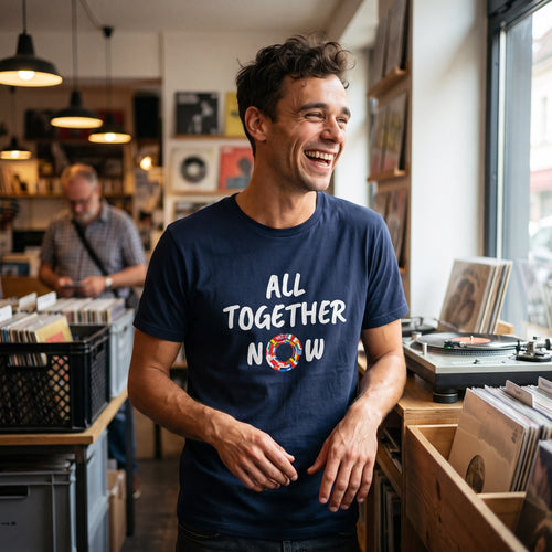 Man laughing in a record shop wearing the navy All Together Now pro-EU t-shirt