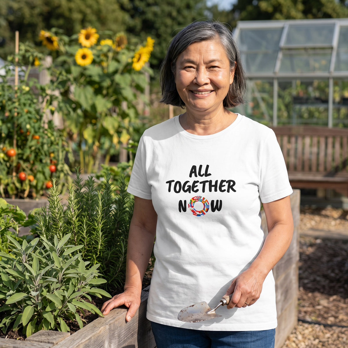 Woman in a community garden wearing the white All Together Now t-shirt with black lettering and a ring of European flags