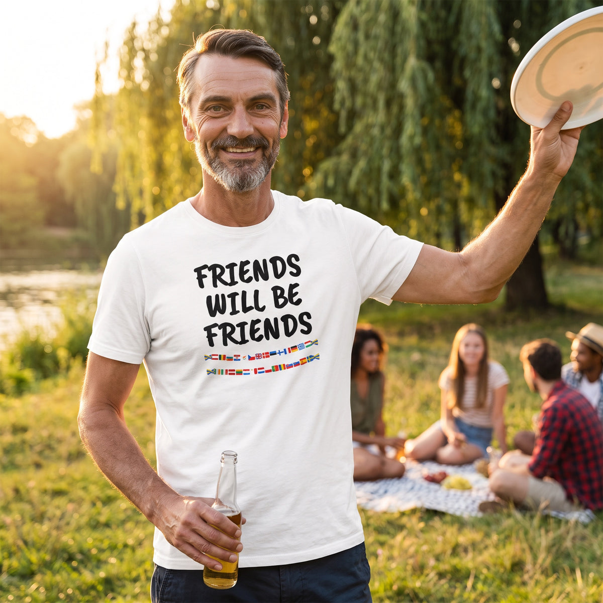 Man at a riverside picnic in a white Friends Will Be Friends t-shirt with black print