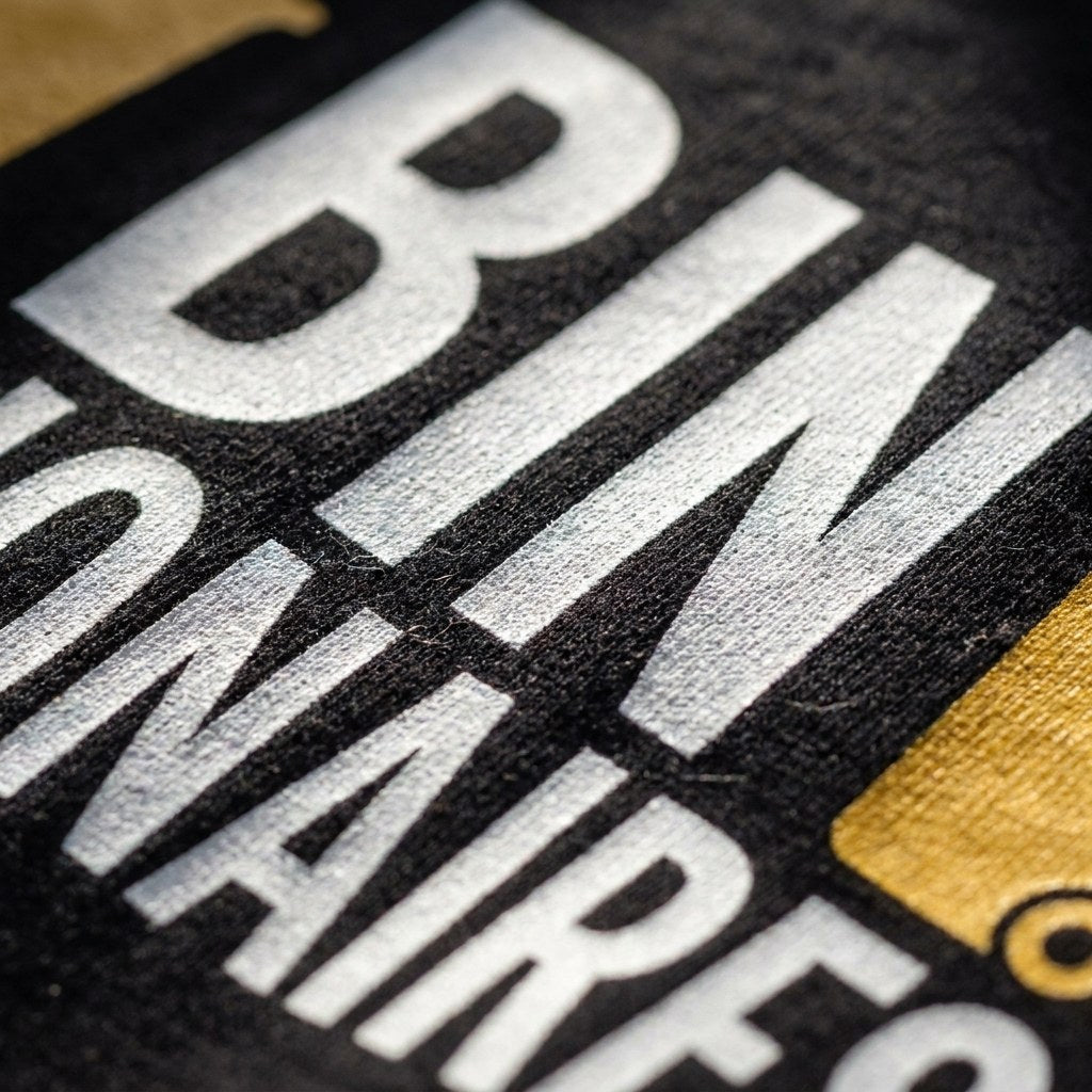 Close up of the white and gold ink Bin Billionaires print on black cotton, showing the fabric weave