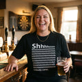 Woman in a black Shhh Nobody Cares t-shirt laughing in a pub