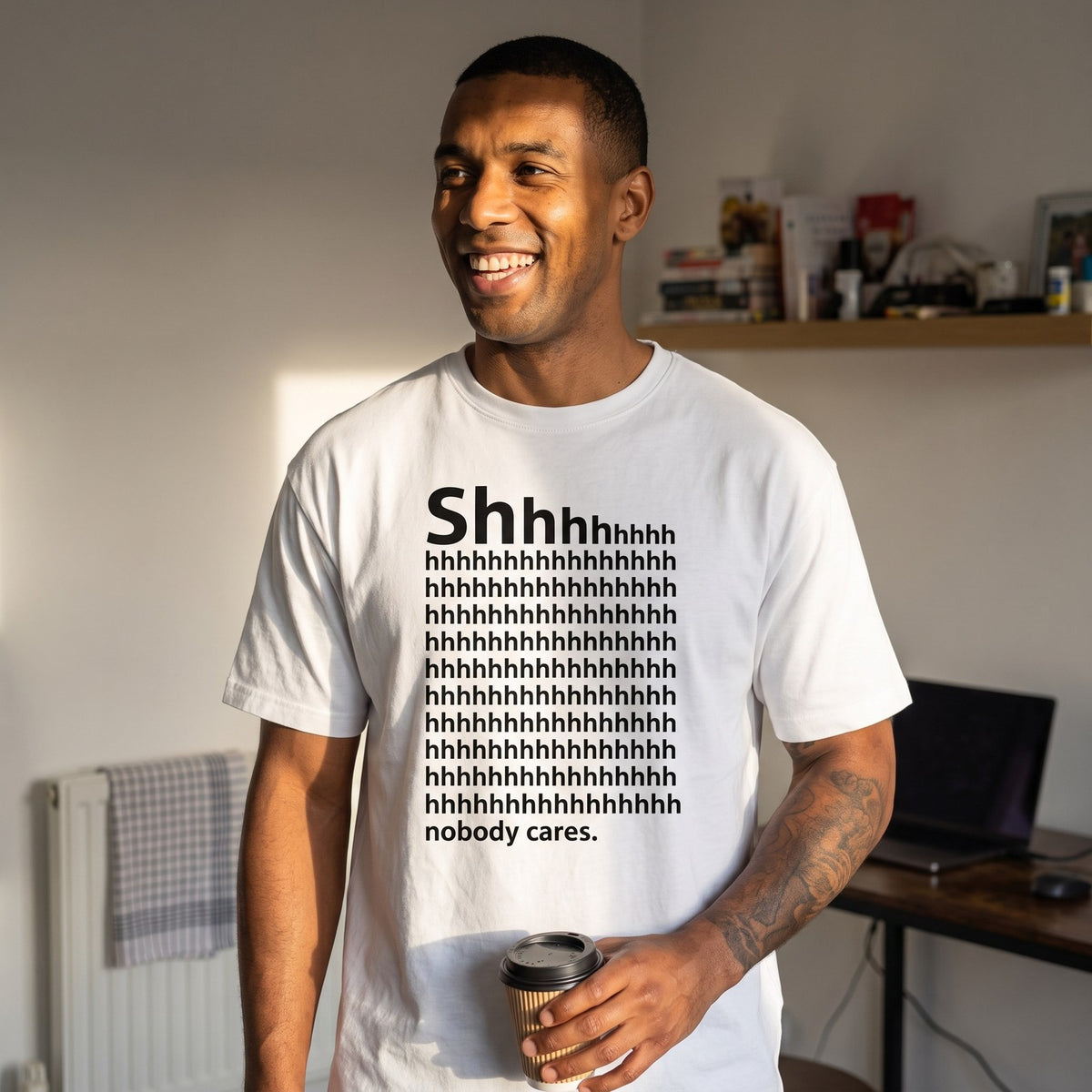 Man in a white Shhh Nobody Cares t-shirt in a living room