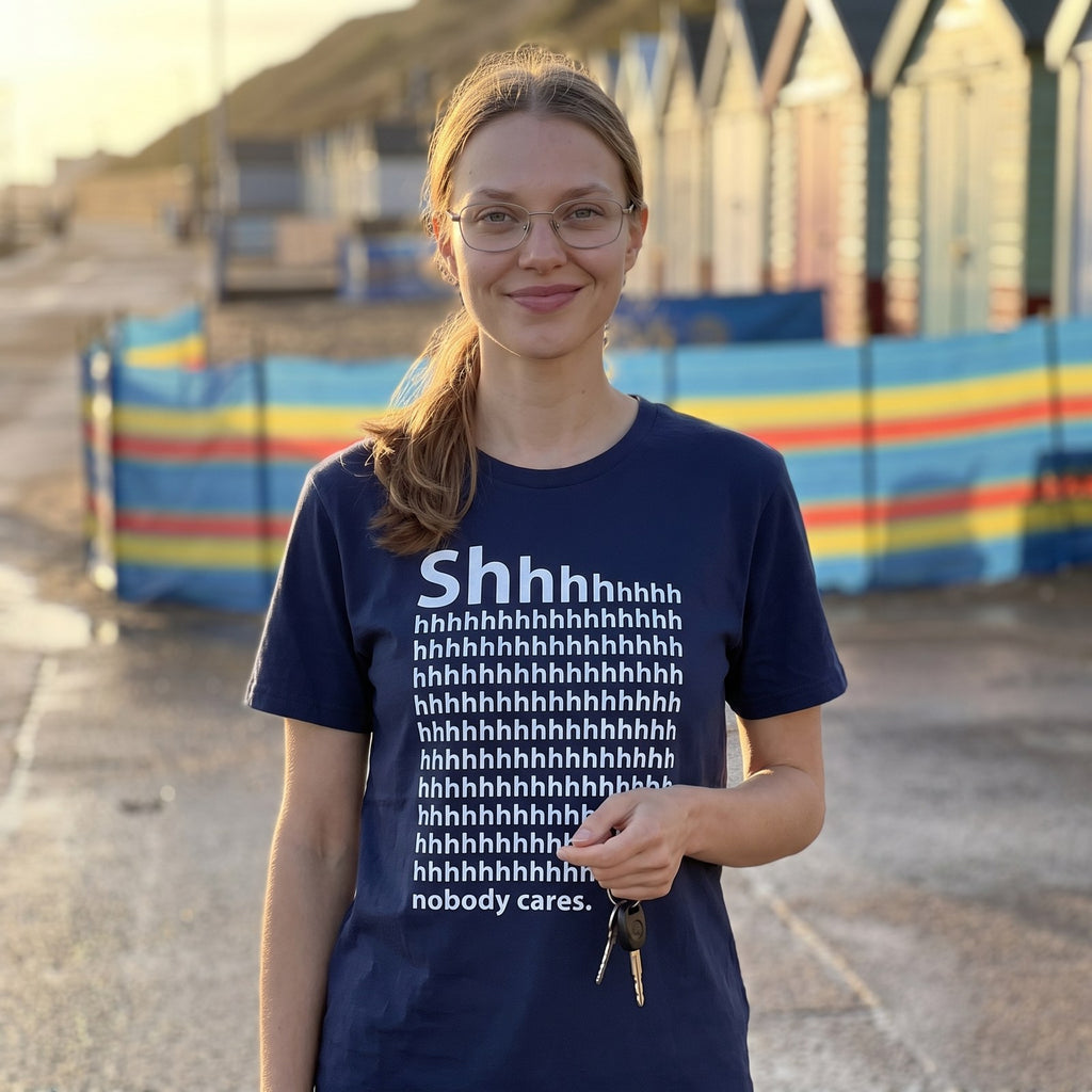 Woman in a navy Shhh Nobody Cares t-shirt on a seaside promenade