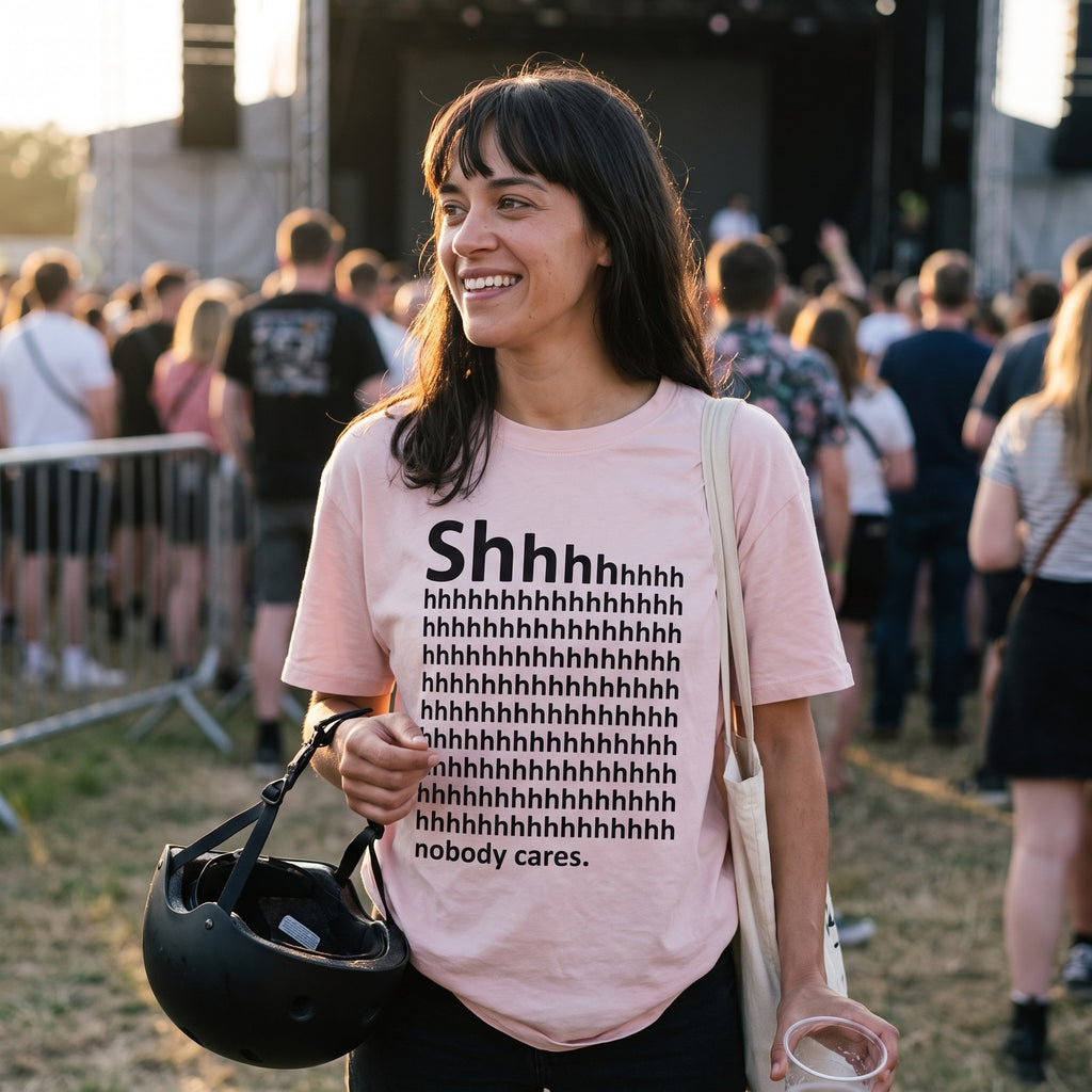 Woman in a pink Shhh Nobody Cares t-shirt at an outdoor gig