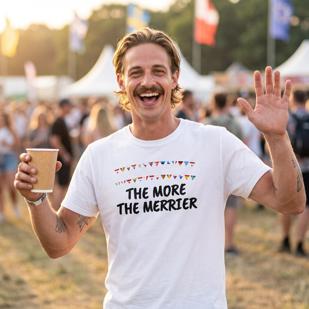 Man waving at a music festival wearing the white The More the Merrier t-shirt with black lettering