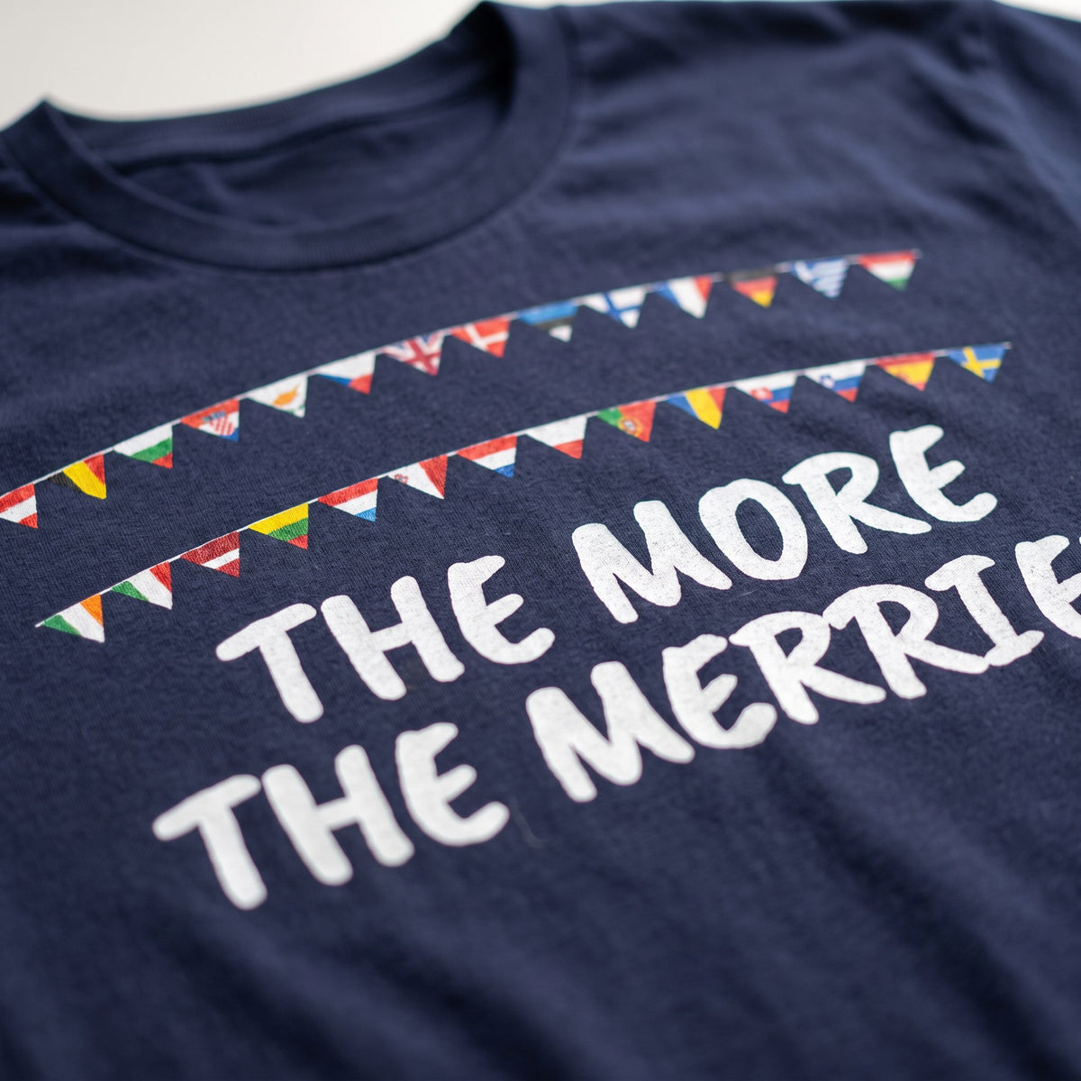 Close-up of The More the Merrier print on a navy t-shirt, hand-painted European flag bunting, showing cotton texture