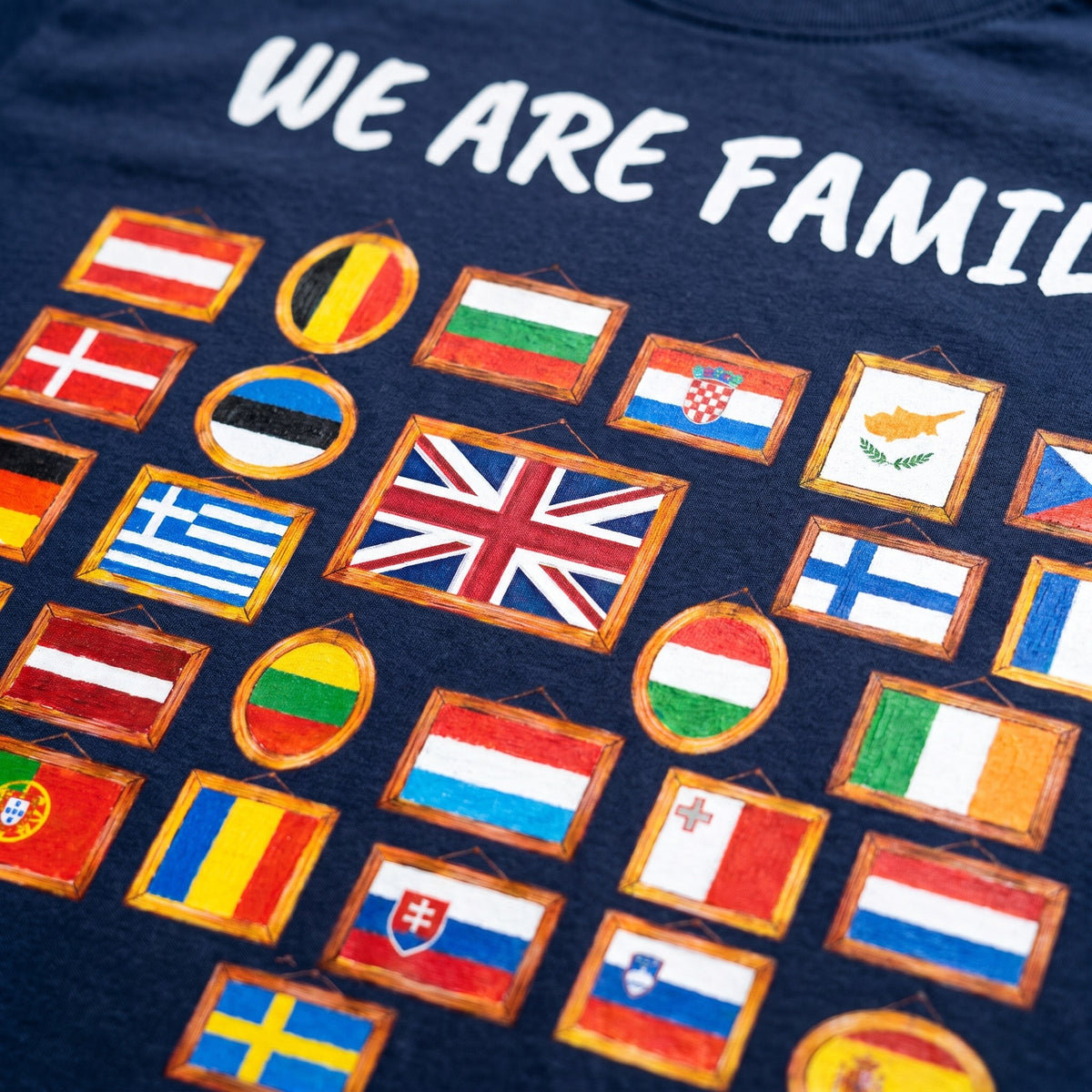 Close-up of the We Are Family print on a navy t-shirt, 28 hand-painted flags in picture frames, showing cotton texture and ink detail