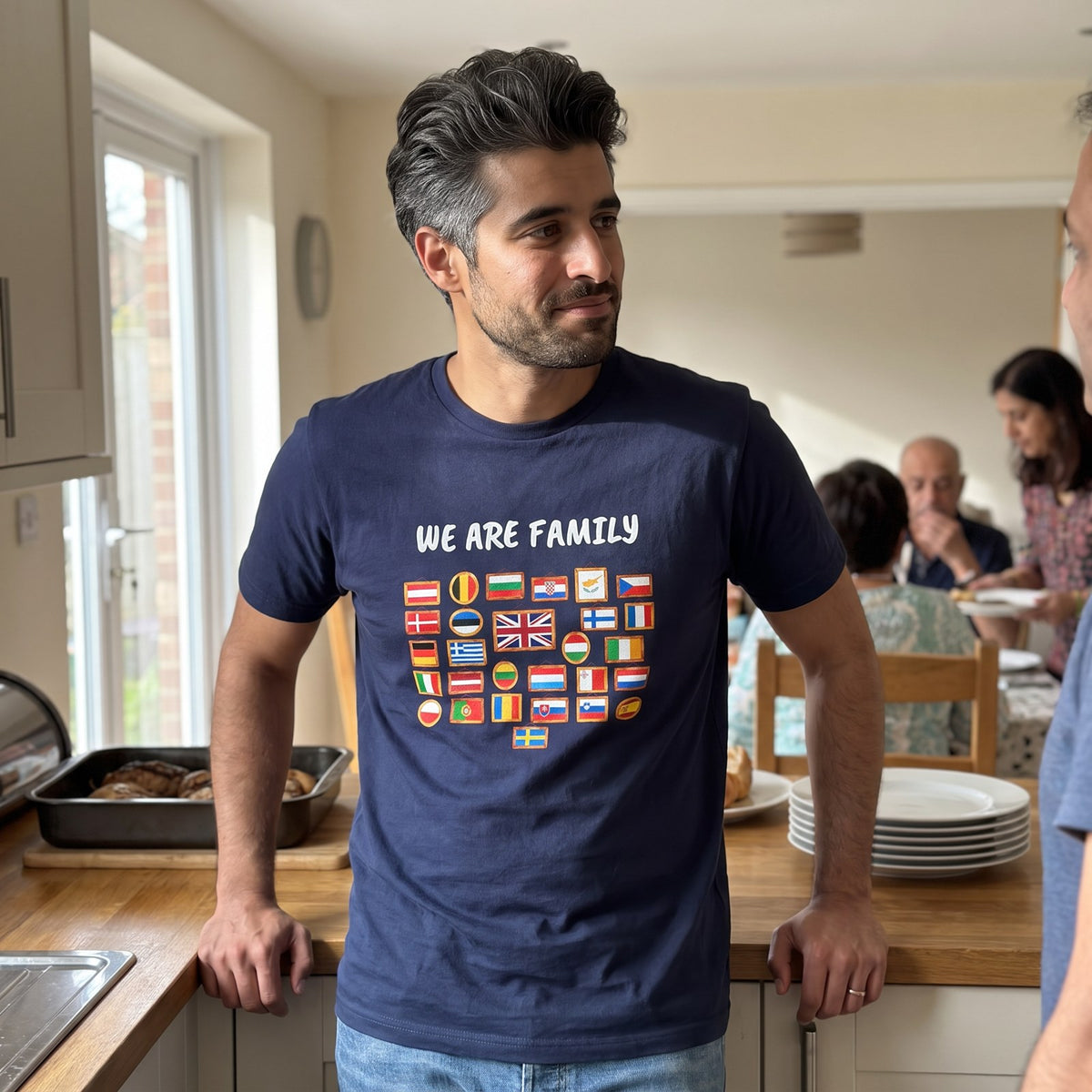 Man leaning on a kitchen counter at a family Sunday lunch wearing the navy We Are Family European flags t-shirt, Very Brexit Problems