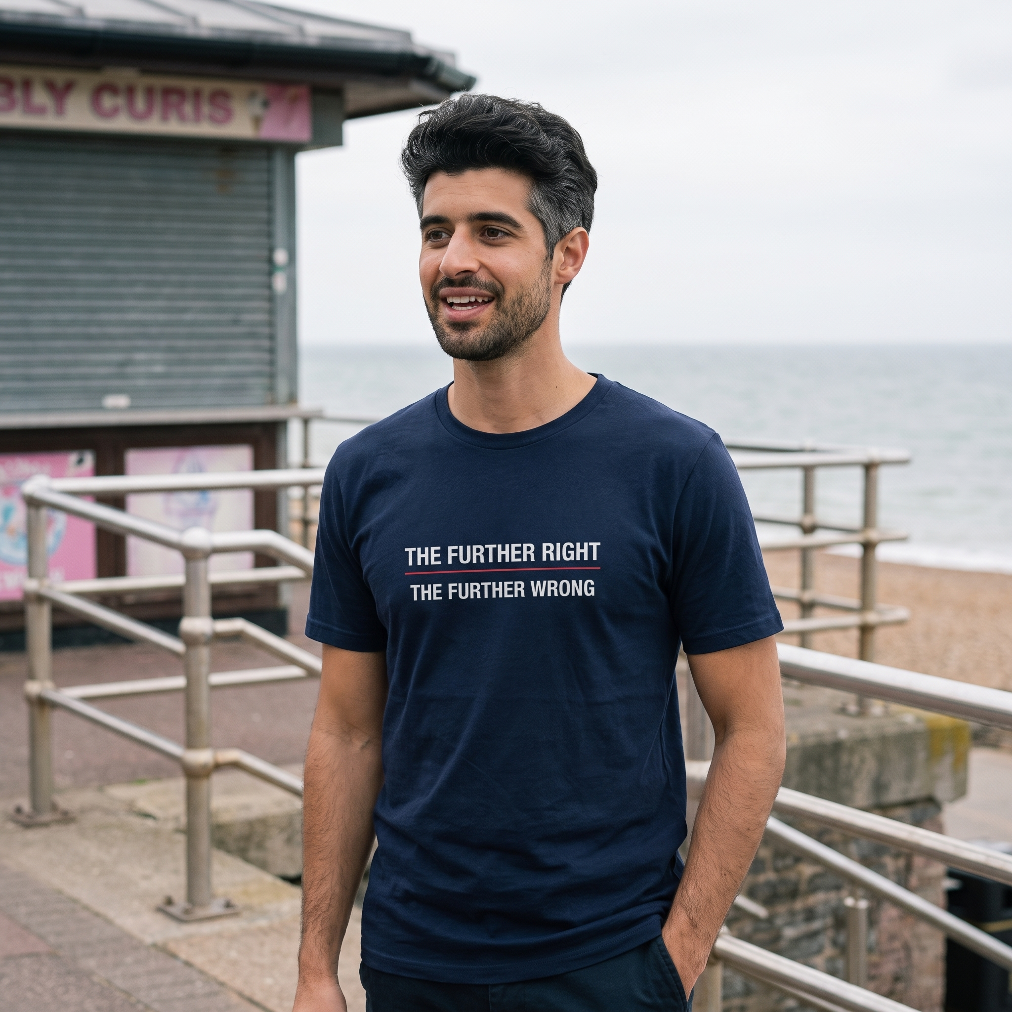 Man wearing a navy The Further Right, The Further Wrong t-shirt on a seaside promenade