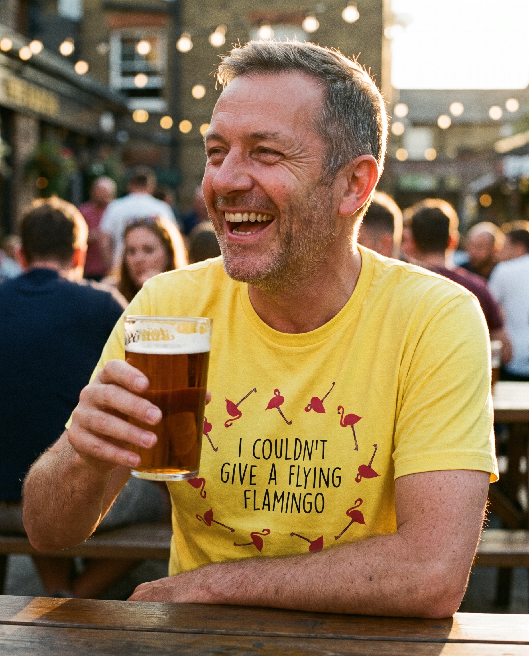 Man laughing in a pub beer garden holding a pint, wearing the yellow I Couldn't Give a Flying Flamingo t-shirt, print close and legible, Very Brexit Problems