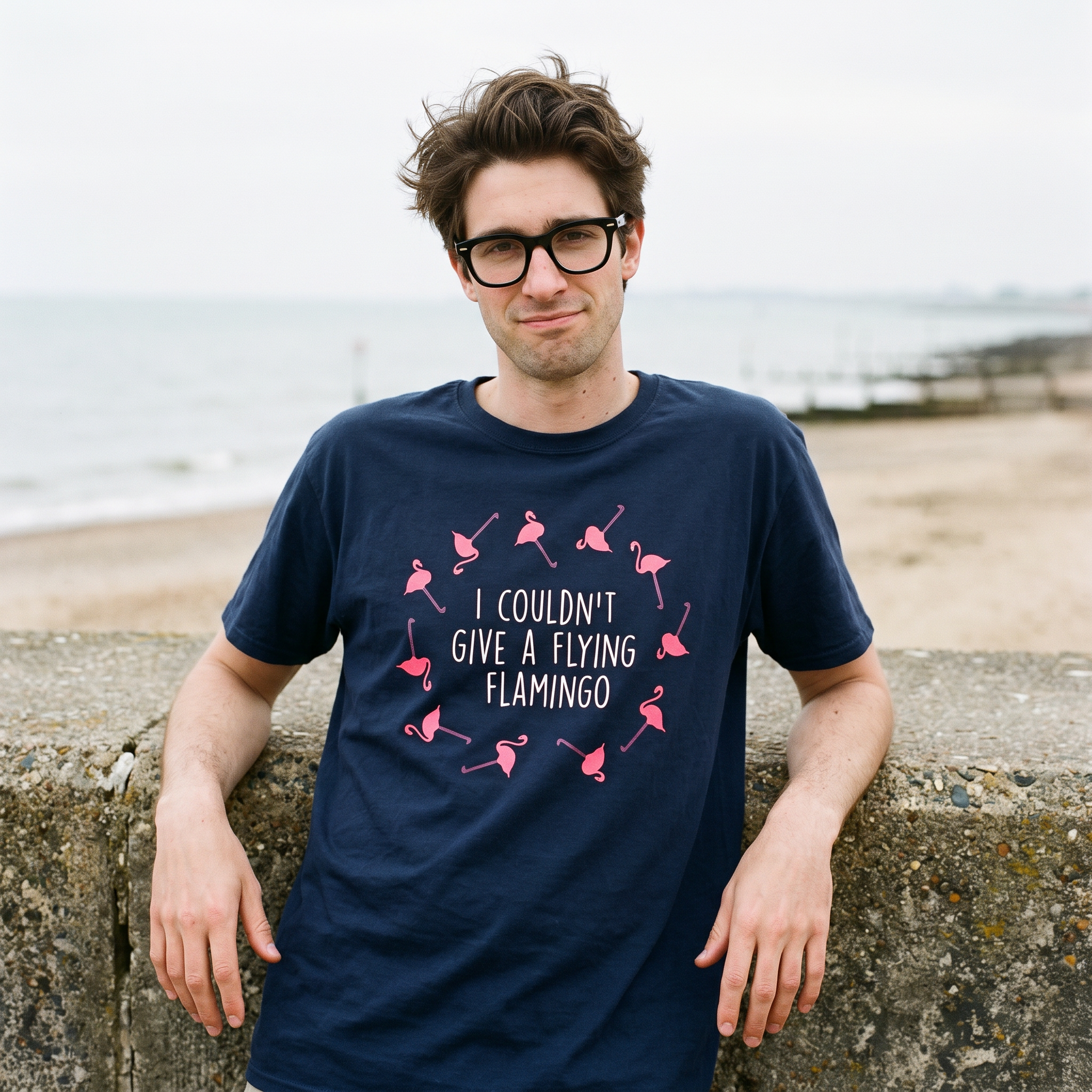 Man in a navy I Couldn't Give a Flying Flamingo t-shirt on a beach beside a low sea wall, Very Brexit Problems